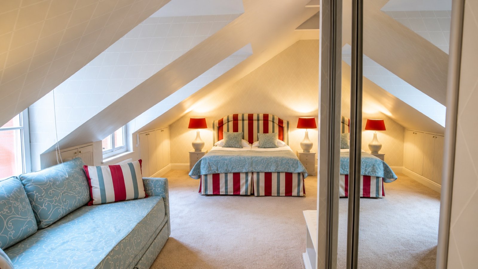 An attic bedroom with a striped headboard and blue sofa